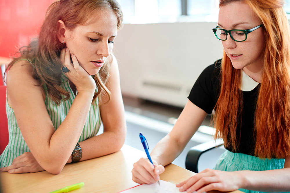 Two women sat together with one lady assessing the others piece of work