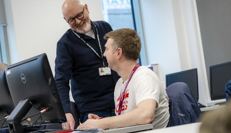 Photograph of a member of staff and student in conversation in a classroom setting.