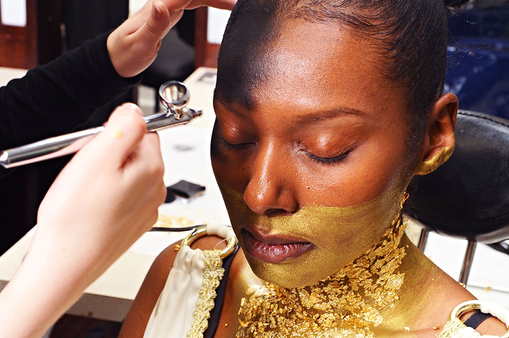 A woman having theatrical, gold make-up applied