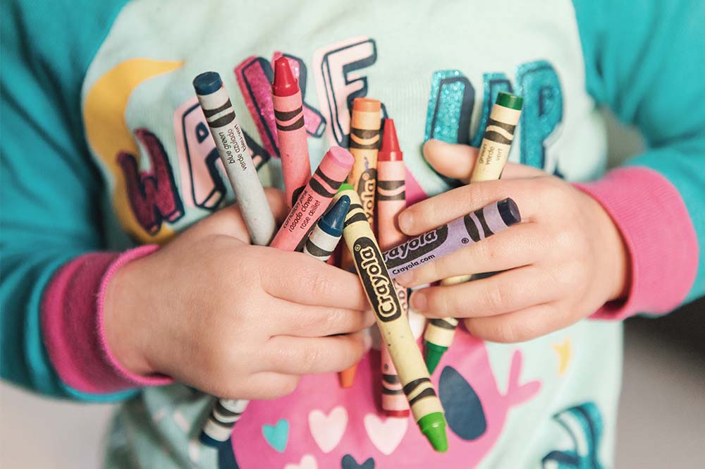 A toddler holding lots of colourful crayons