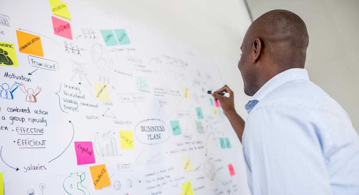 A man writing an organised, strategic business plan on a whiteboard.