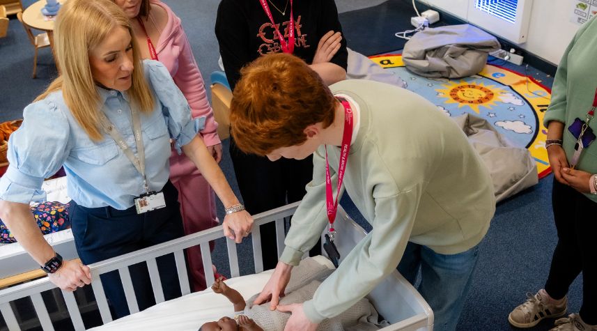 Students taking part in an early years childcare lesson at The Manchester College, practising baby care using a crib and doll.