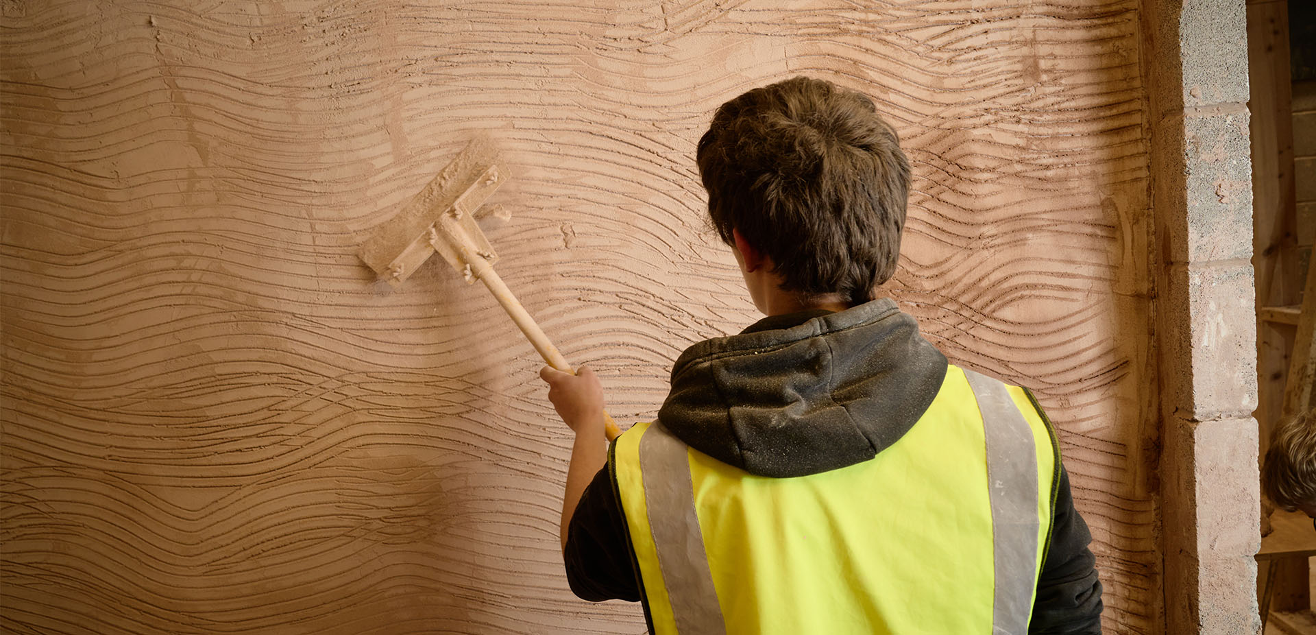 Over-the-shoulder view of a learner plastering a wall