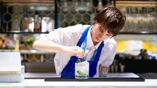 Photograph of a student from The Manchester College preparing a drink in a restaurant bar.