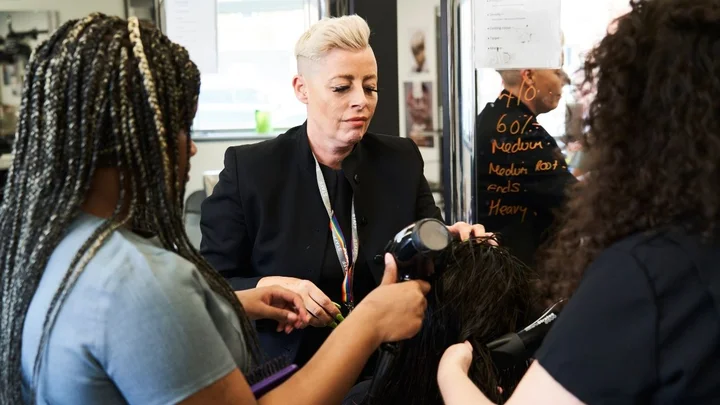 Hairdressing learners working together on a blow‑drying and styling activity in a salon training session.
