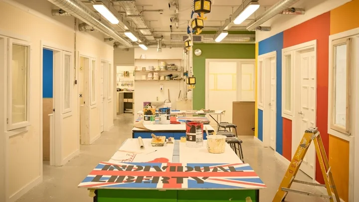 A brightly lit painting and decorating workshop featuring colourful practice walls, workbenches with paint supplies, and tools set up for training activities.