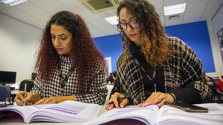 Two adult students reading a textbook