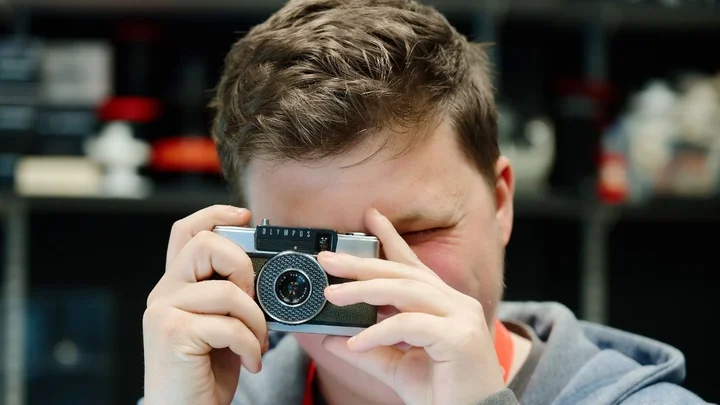 A photography learner holding a camera up to capture a shot in a studio workspace.