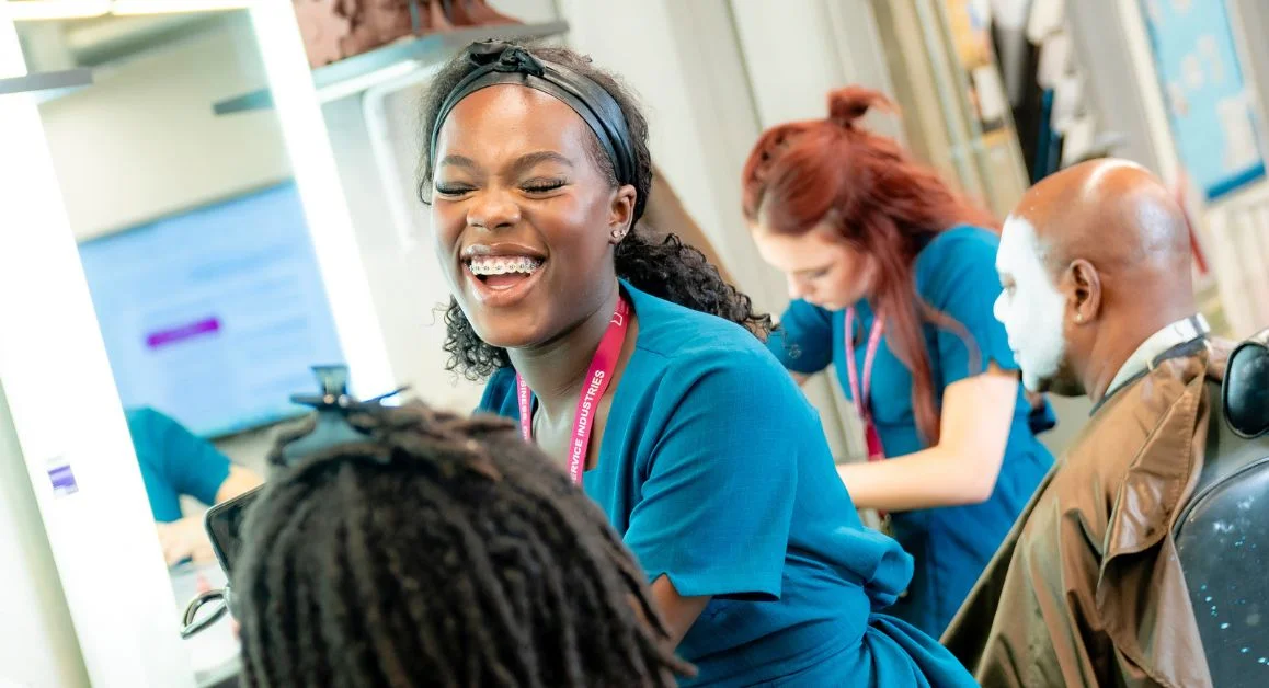 Hair and beauty learners working in a training salon at The Manchester College, practising make-up techniques at individual workstations with mirrors.