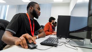 A side profile view of a student from The Manchester College sat at a computer while holding the computer mouse.