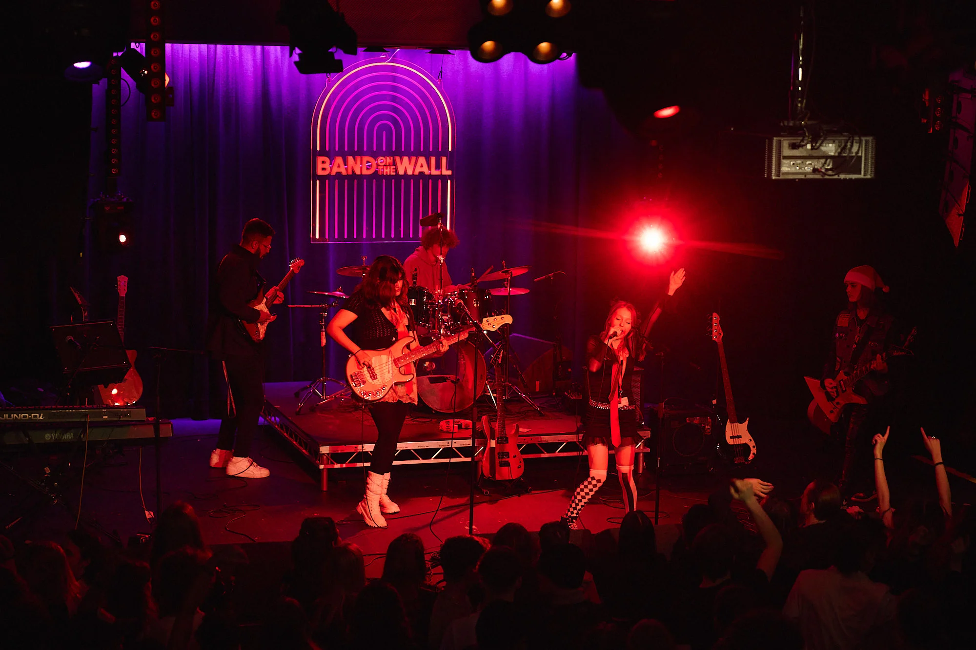 Live band performing on a stage with red and purple lighting in front of an audience.