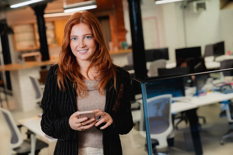 Person standing in a modern office environment while holding a smartphone.