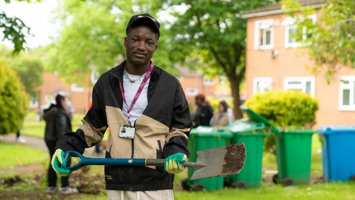 A learner taking part in an outdoor foundation learning session, holding a shovel in a community garden area.