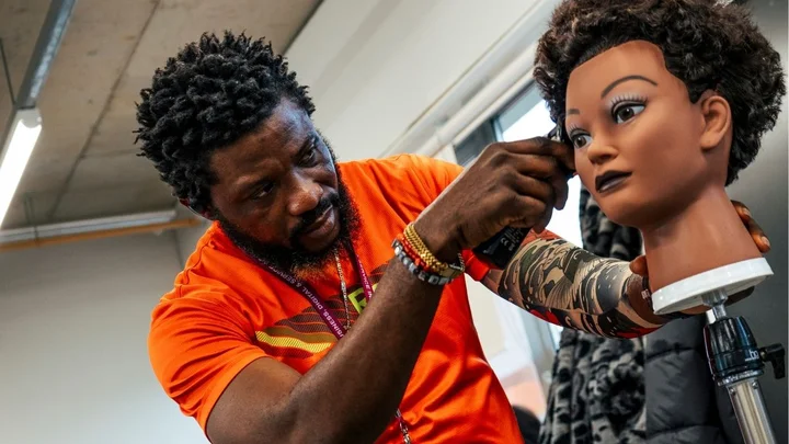 A barbering learner practising clipper work on a training mannequin during a hands‑on session.