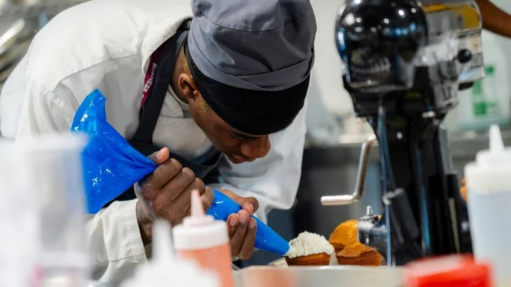 A catering learner piping icing onto cupcakes during a practical baking session in a professional training kitchen.