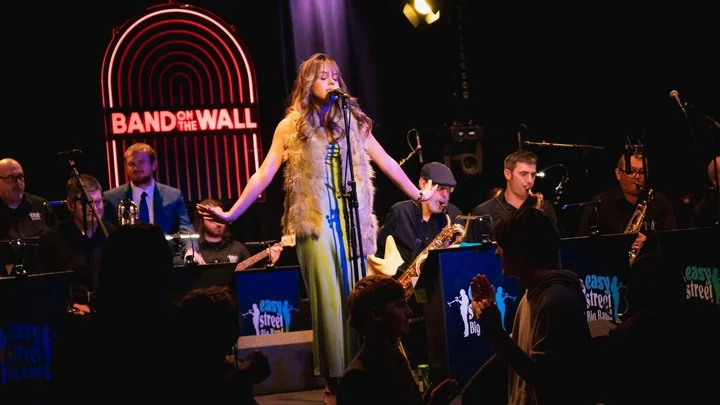 A live big band performance at Band on the Wall, featuring a vocalist centre‑stage with musicians playing brass and wind instruments in front of an audience.