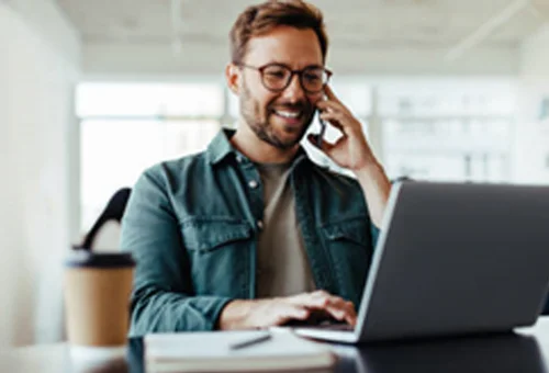 A man talking on the phone while using a laptop