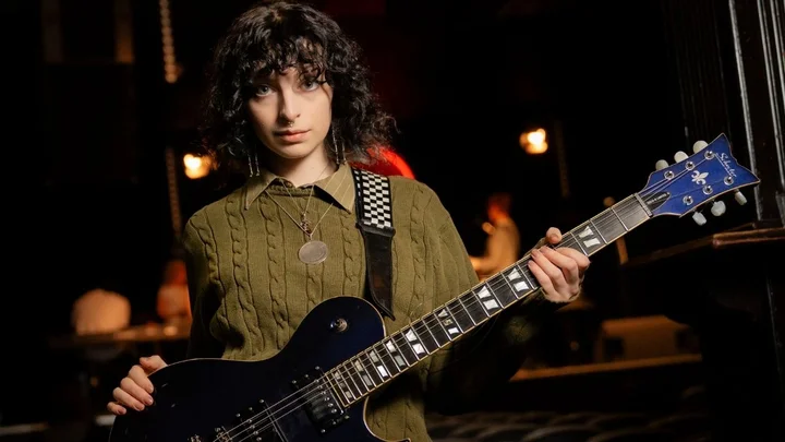 A music learner holding an electric guitar on stage at Band on the Wall, preparing for a live performance.