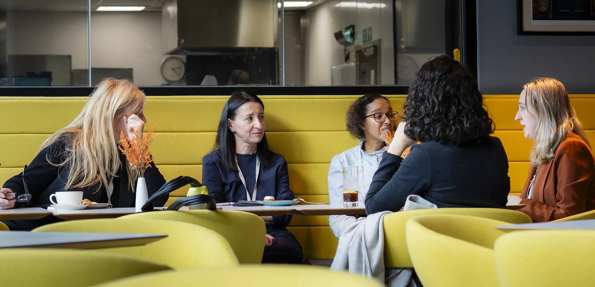 Group of people seated around a table in a modern seating area, taking part in a discussion over drinks and documents during a meeting.