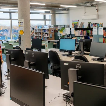Computer suite and library at The Manchester College Harpurhey Campus with rows of desktop computers, study desks and bookshelves in a modern learning environment.