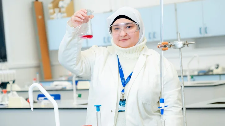 Science student from The Manchester College wearing safety goggles and a lab coat holding a flask of red liquid during a practical experiment
