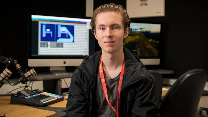 A learner in a digital media studio sitting at a desk with professional microphones, audio equipment, and dual monitors displaying creative software.