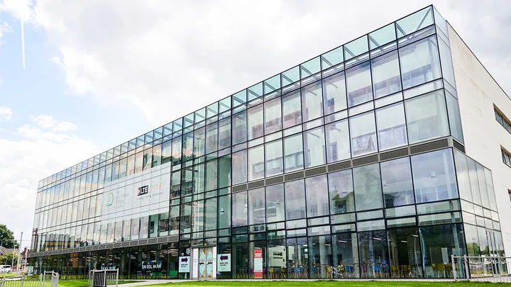 Exterior view of The Manchester College Wythenshawe Campus, showing a large glass‑fronted building with multiple floors, green lawn and main entrance signage.