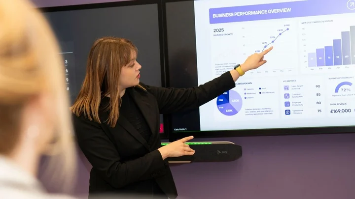 Person presenting business performance data on a large digital screen during a business learning session.