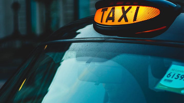 A lit up Taxi sign on a car