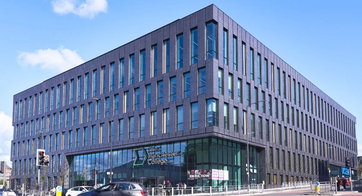 Exterior of The Manchester College City Centre Campus, a modern multi-storey building with dark brick, tall vertical windows, and a glass entrance on a city street.