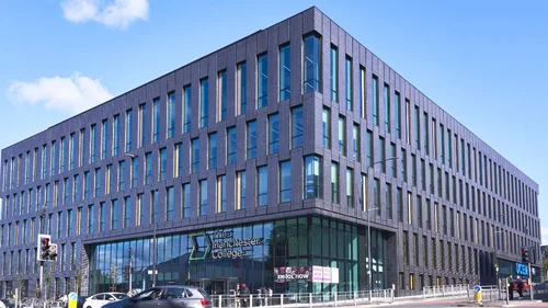 Exterior of The Manchester College City Centre Campus, a modern multi-storey building with dark brick, tall vertical windows, and a glass entrance on a city street.