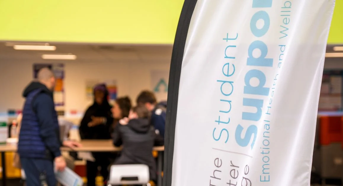 A Student Support banner in the foreground with people gathered and receiving guidance at a support desk in the background.