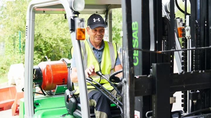 A forklift learner operating a green counterbalance truck while manoeuvring the controls during a practical training session.
