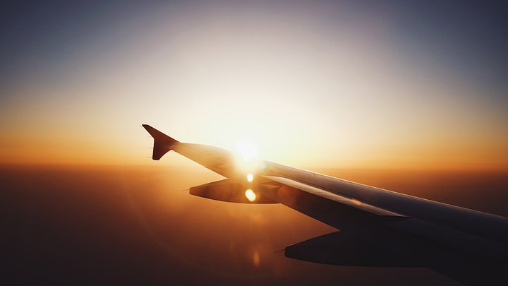 A view of a plane wing with a sunset on the horizon