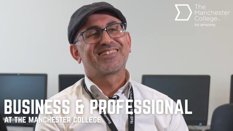 Person wearing glasses, a flat cap and a lanyard seated in a computer classroom, with text reading “Business & Professional at The Manchester College”.