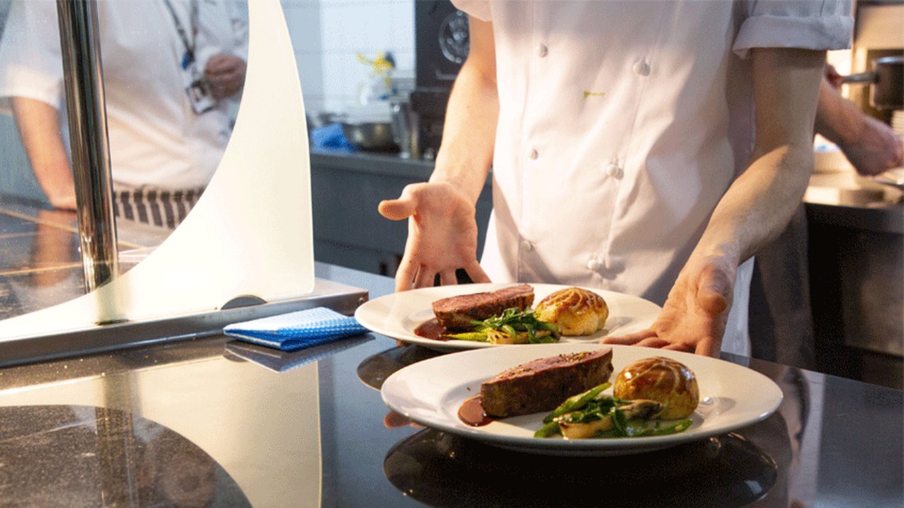 A student chef presenting two plates of well presented, freshly cooked food.