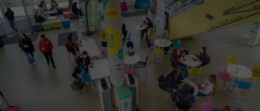 An overhead view of students sitting and walking through a bright common area at The Manchester College with colourful chairs, welcome banners and large windows.