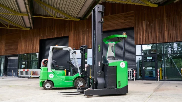 Two green forklifts parked outside a training facility, including a counterbalance truck and a reach truck.