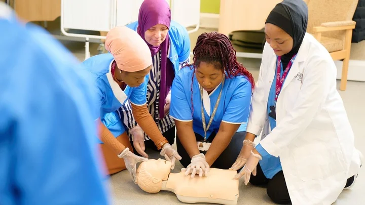 Health and social care learners practising CPR on a medical training manikin during a practical emergency response session.