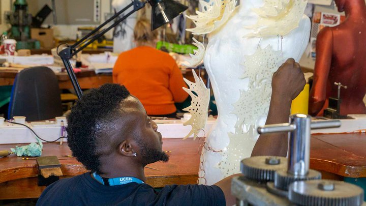 A student stitching costume elements on a dummy