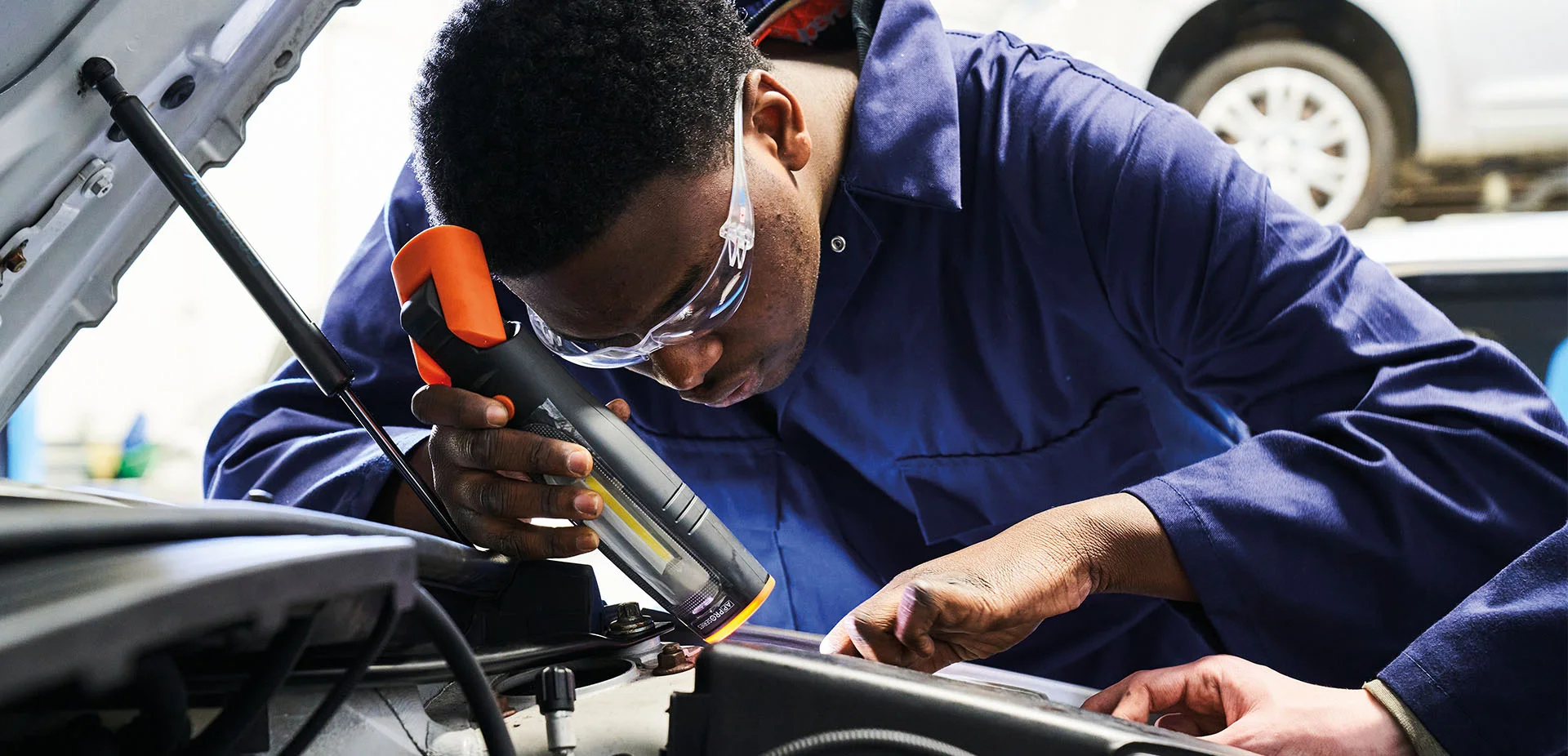 Automotive learner at The Manchester College using diagnostic equipment while working on a vehicle engine in a workshop.