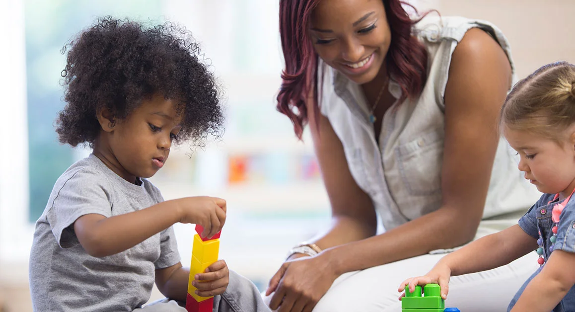 Adult and two children playing with colourful building blocks.
