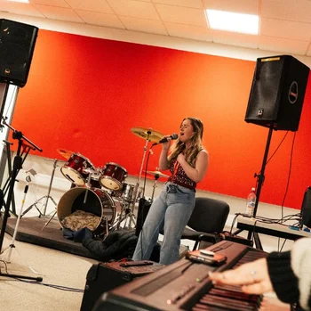 Music student rehearsing vocals in a band practice room at The Manchester College, with drums, keyboards and professional equipment.