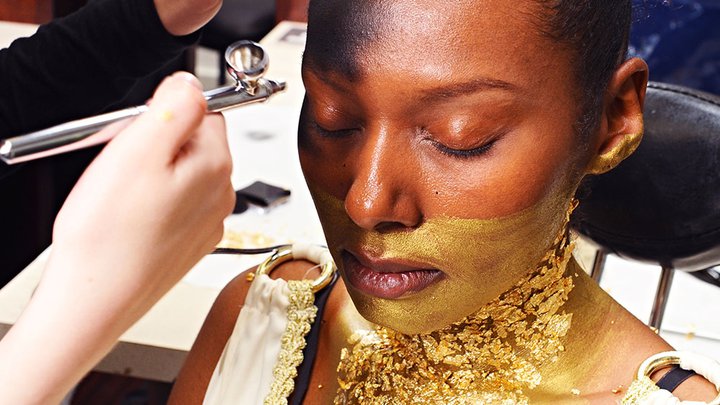 A woman having theatrical, gold make-up applied