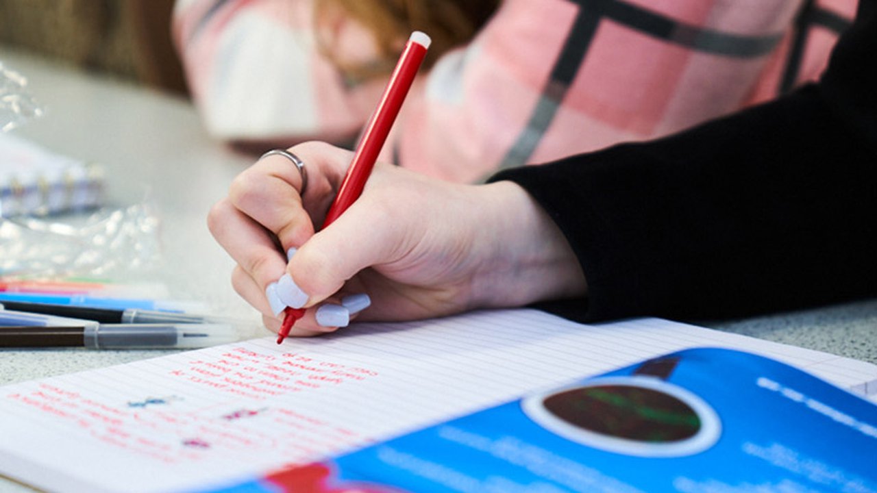 Photograph of a student from The Manchester College writing in a note pad in red ink.