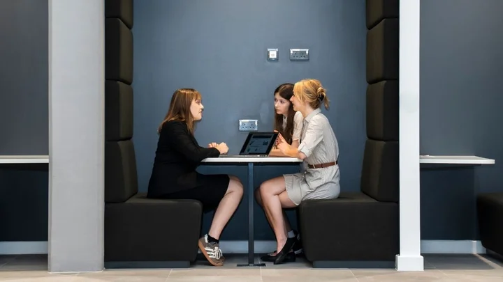 Business and Professional Services learning area showing learners seated in a modern meeting booth using a laptop for collaborative discussion and group work.