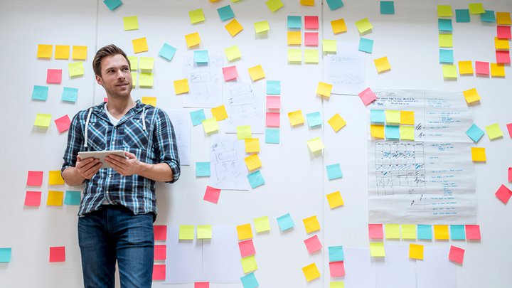 Man standing next to a white board with different coloured post it notes on