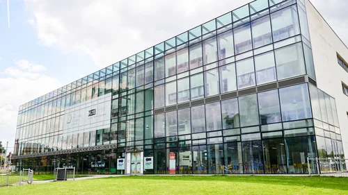 Exterior of The Manchester College Wythenshawe Campus, a modern glass-fronted building with large windows and a green lawn in front.