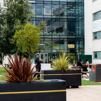 Courtyard at The Manchester College Harpurhey Campus with landscaped planters, benches and a modern glass-fronted college building in the background.