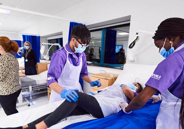Healthcare learners at The Manchester College practising patient handling techniques in a clinical training environment.